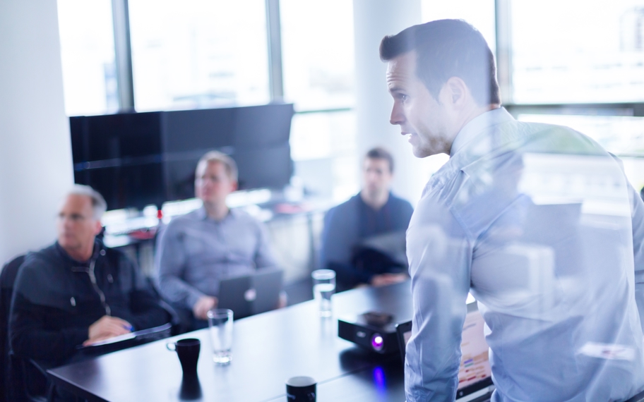 Møde mellem fire personer, hvor den ene står op og snakker