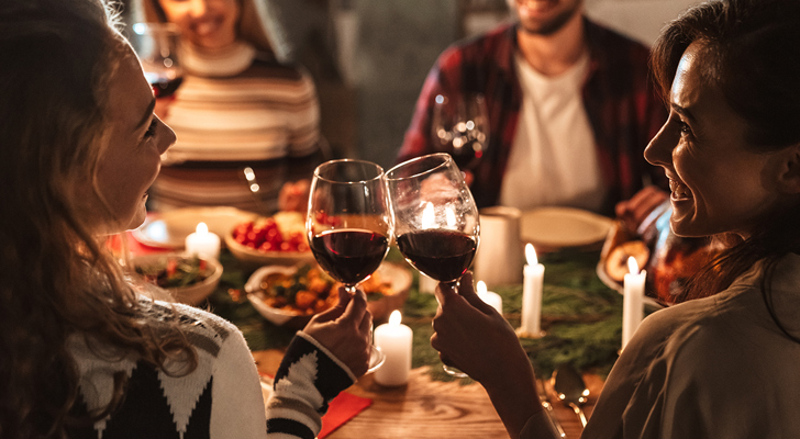 To kvinder skåler i vin til julefrokost med to personer siddende overfor dem