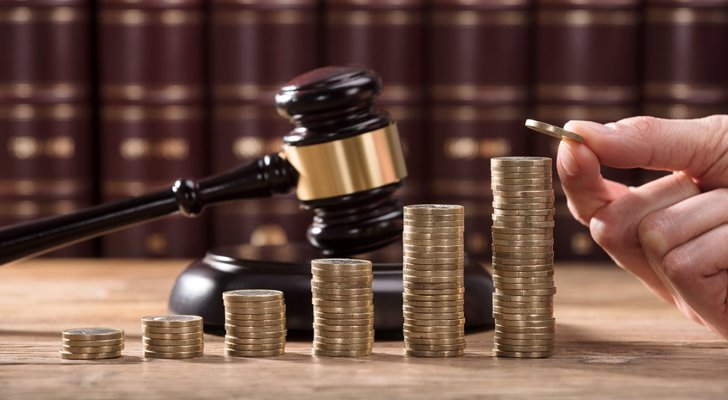 Hånd stabler mønter med dommerhammer bagved mønterne - kompensation 