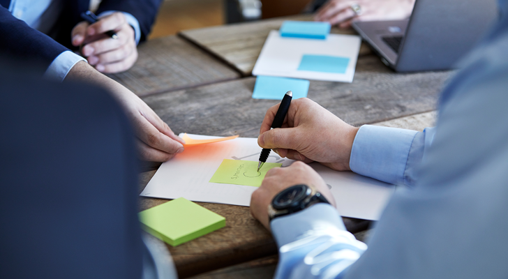 Møde mellem fire personer hvor der bliver skrevet på papir og post-it